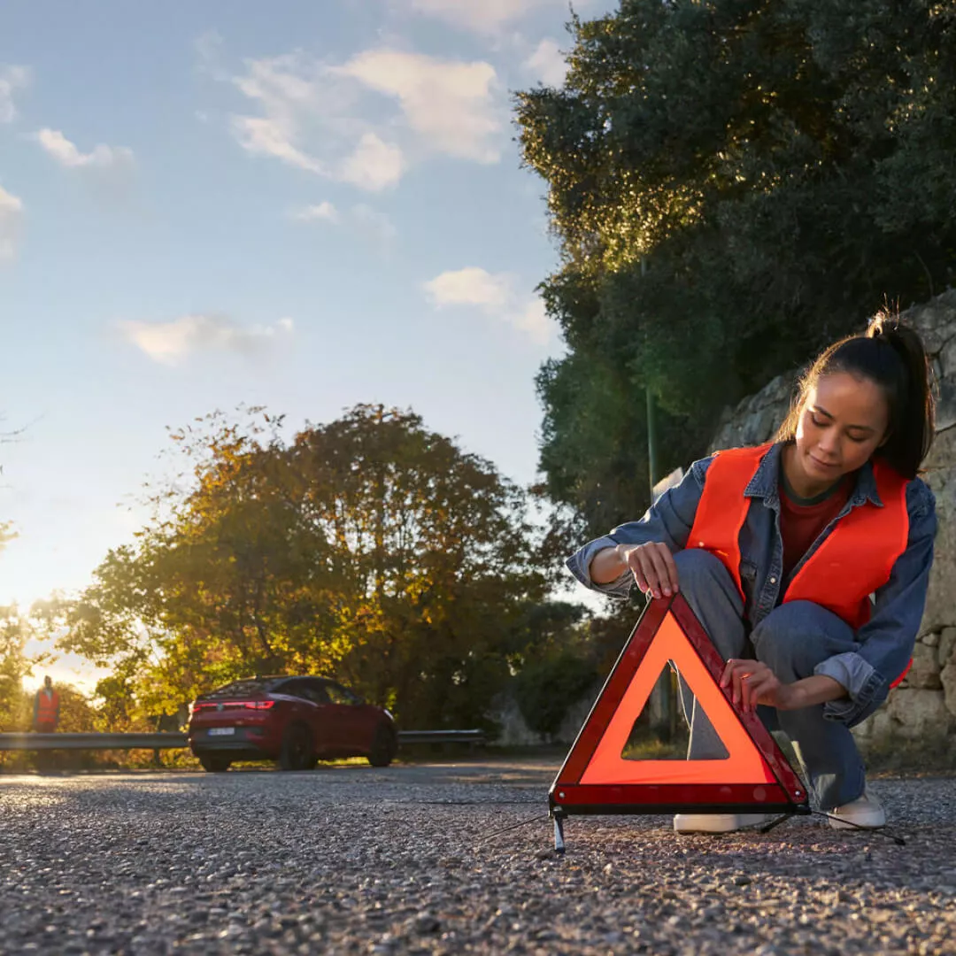 Una mujer colocando el triangulo de emergencia en una carretera
